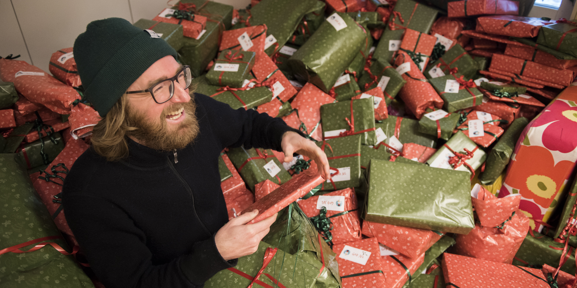 Skrattande kille sitter i ett hav av julklappar