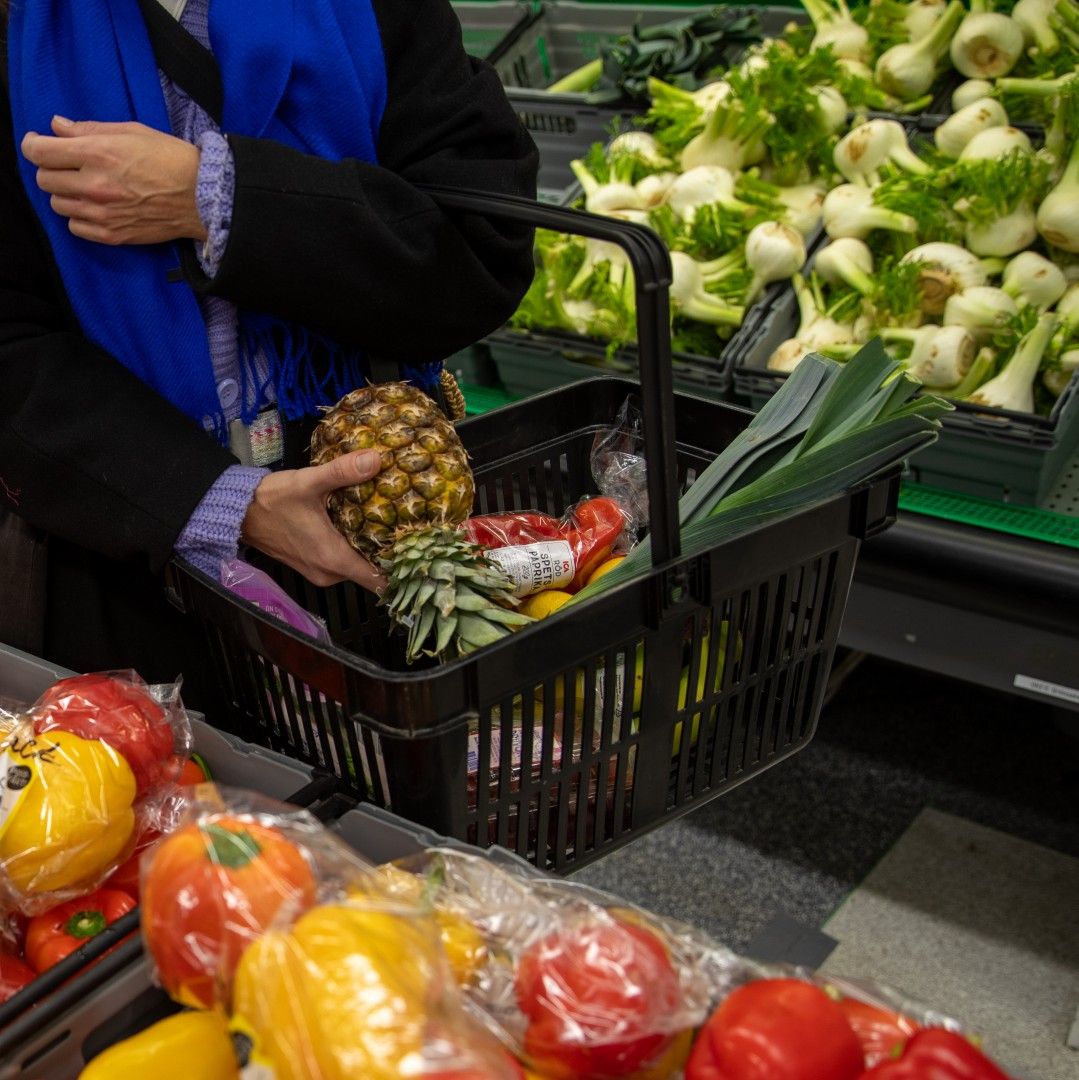 Människa som håller en varukorg fylld med frukt och grönt