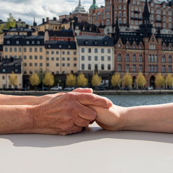 Två människor håller händerna med Stockholm i bakgrunden.