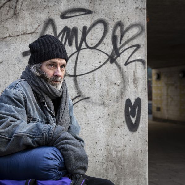 En hemlös man sitter vid en gångtunnel, på betongväggen är det klotter