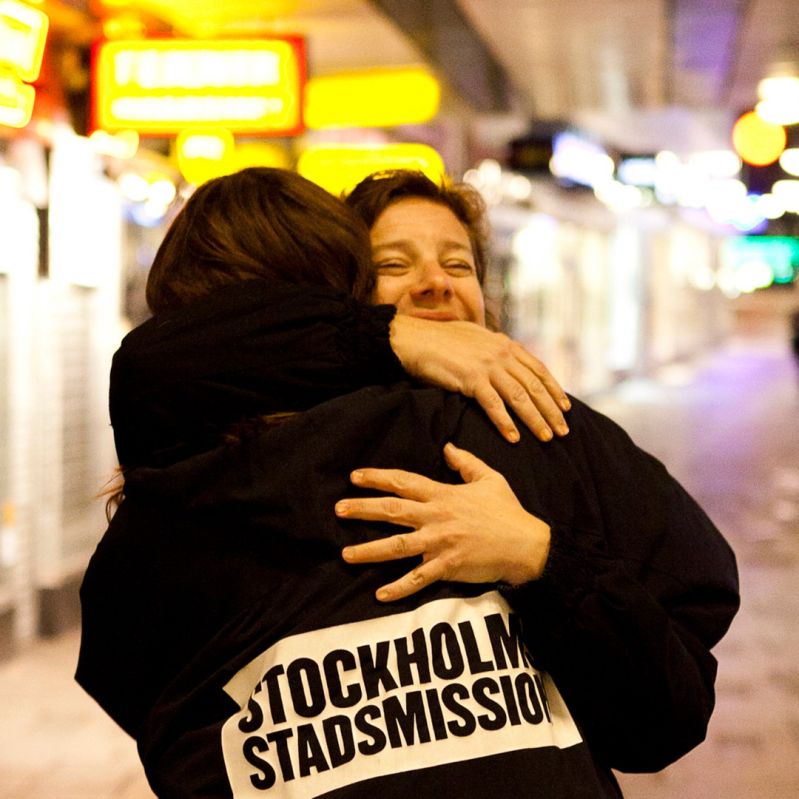 En medarbetare från Stockholms Stadsmission kramar en människa på gatan.