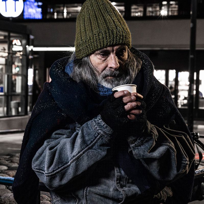 En man sitter och fryser på en bänk bredvid tunnelbanan.